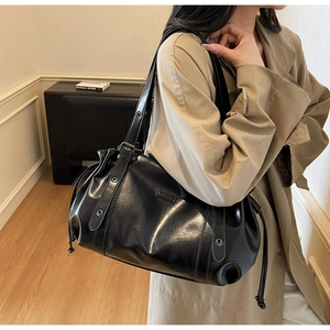 Detail of black glossy leather shoulder bag with drawstring closure and metal plate