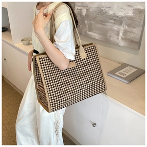 Detail of a large houndstooth tote bag with canvas straps and a leather logo patch