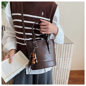 Detail der karamellbraunen matten Beuteltasche mit Markenlogo und Ethno-Perlenanhänger