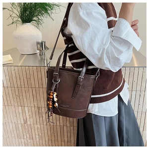 Detail einer dunkelbraunen matten Eimer-Tasche aus Leder mit buntem Perlenanhänger