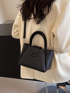 Sac seau noir en cuir texturé porté avec un tailleur beige par un mannequin femme