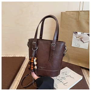 Nahaufnahme der braunen Eimer-Handtasche mit einem bunten Quastenanhänger aus Holzperlen