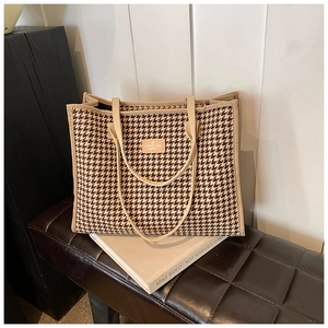 Detail of checkered canvas tote bag with brown leather patch and woven handles