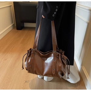 Detail of dark brown tote bag showing side drawstrings and adjustable strap buckles