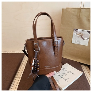 Detail der braunen Leder-Beuteltasche mit Holzperlen-Anhänger und Logo-Schriftzug