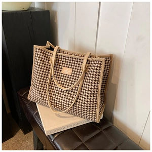 Detail of houndstooth tote bag featuring a leather patch on a textured canvas surface