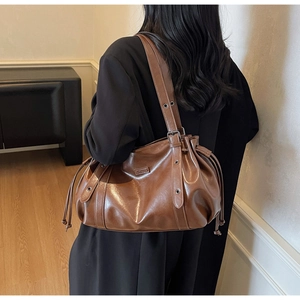 Detail view of brown leather shoulder bag with side drawstring and metal logo plate