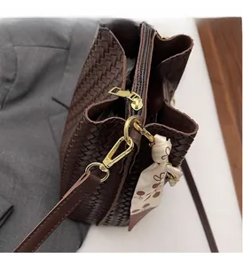 Detail of dark brown woven leather bucket bag with gold hardware and floral scarf accent