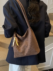 Brown leopard embossed suede tote bag with wooden bead tassels shown on a shoulder