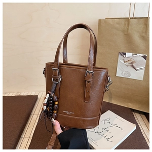 Detail einer braunen Eimertasche aus Leder mit Holzperlen und Quastenanhänger mit Schultergurt