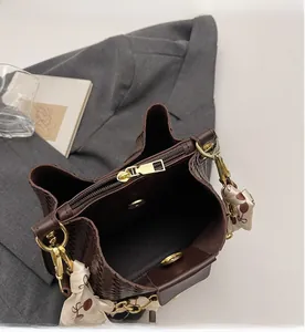 Close-up of brown woven bucket bag featuring gold zipper and silk scarf detail