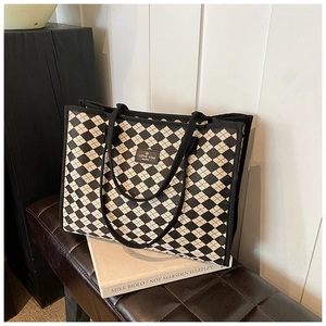 Detail of checkered canvas tote bag with leather logo patch on a brown bench