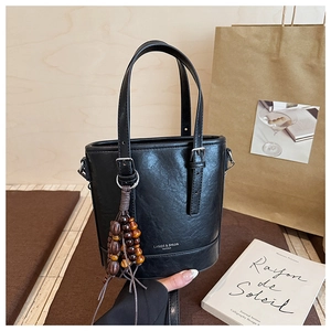 Detail der schwarzen Leder-Beuteltasche mit weißem Logo und Holzperlenanhänger auf Kissen