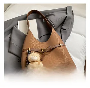 Detailed view of leopard print tote bag with bear charm on grey blazer backdrop