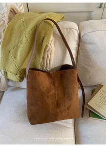 Nahaufnahme der braunen Veloursleder-Tote-Bag mit Lederriemen auf weichem Sofa