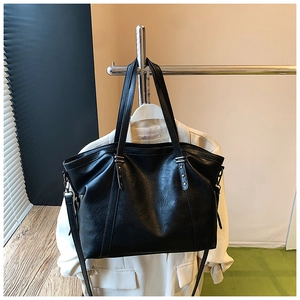 Détail du grand sac cabas noir en similicuir avec rivets étoilés sur fond de blazer