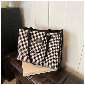 Detail shot of black and white houndstooth tote bag with logo on a leather bench