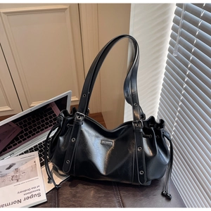 Detail of black glossy leather tote bag with drawstring design and metal logo plaque