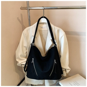 Détail du grand sac hobo noir avec doubles fermetures éclair argentées sur un blazer