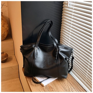 Détail du grand sac cabas en cuir PU noir avec bandoulière amovible sur un support bois