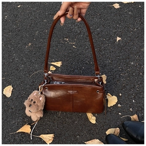 Détail d'un sac à main en cuir marron foncé avec plaque logo et breloque chien