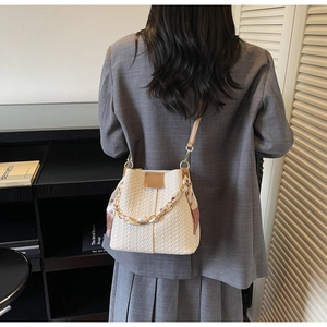 Detail of hand-woven cream bucket bag with gold chain and decorative silk scarf handle