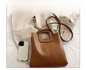 Detail view of brown leather tote bag featuring unique square handle and adjustable strap