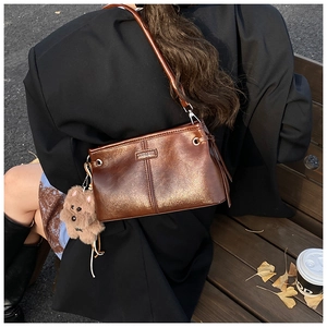 Vue détaillée d'un sac bandoulière marron vintage avec un charm ours sur un banc de parc