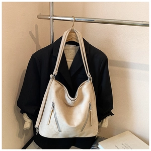 Détail du grand sac cabas beige avec poches zippées devant un blazer noir élégant