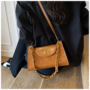 Detail of a brown embossed leather crossbody bag with a chunky gold chain and metal lock