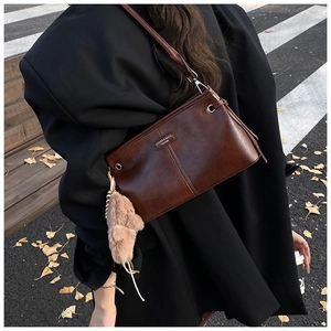 Détail d'un sac bandoulière vintage marron foncé avec un porte-clé en peluche