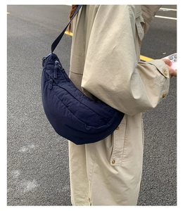 Detail of navy blue half-moon dumpling bag with adjustable strap on a beige trench coat