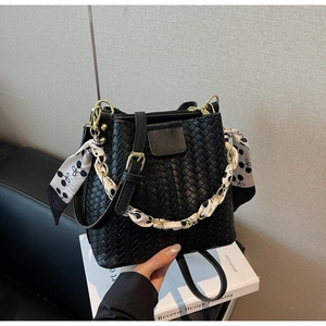 Close-up of black woven bucket bag featuring silk scarf chain strap and zip closure