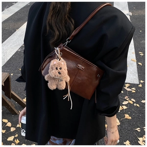 Détail d'un sac à bandoulière en cuir marron foncé avec logo en métal et ours en peluche