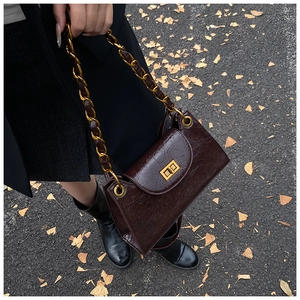 Detail of vintage oil wax leather bag with golden chain strap on autumn leaves