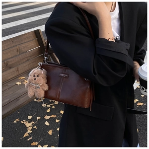 Détail d'un sac à bandoulière en cuir marron avec breloque ours sur un banc en bois