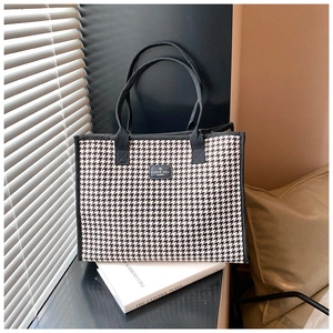 Detail of large houndstooth tote bag with black trim and a stylish logo label