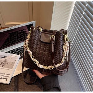 Detailed close-up of a woven dark brown bucket bag with a silk scarf wrapped chain handle