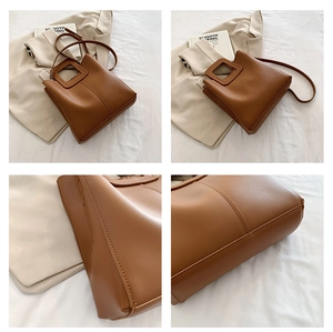 Detail of caramel leather tote bag stitching and square cutout handle on white fabric