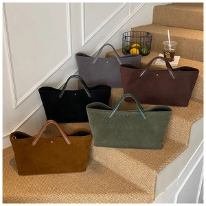 Detail showing five colors of suede tote bags arranged on steps in a lifestyle setting