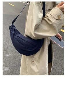 Detail of navy blue crescent nylon crossbody bag worn on a woman's shoulder outdoors