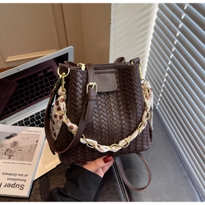 Close-up of brown woven bucket bag featuring a gold chain handle with silk scarf detail