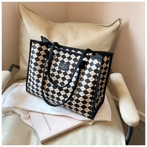 Detail of checkered canvas tote bag featuring stitched square logo on armchair