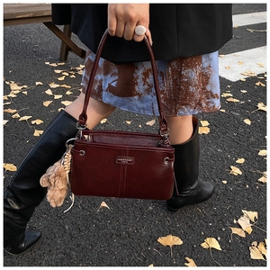 Détail du sac à main en cuir bordeaux avec coutures verticales et breloque ours peluche