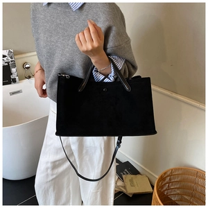 Black matte suede tote bag shown in a cozy lifestyle setting with shoulder strap