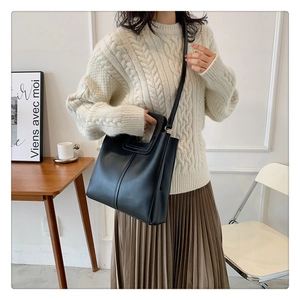 Minimalist black leather tote bag featuring unique hollow handle and adjustable strap detail