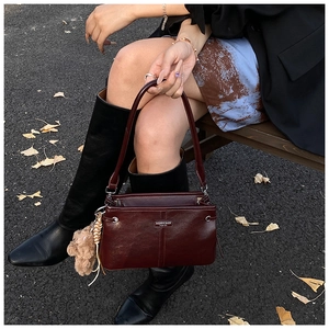 Détail du sac à main en cuir bordeaux brillant avec plaque logo et charm d'ours