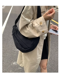 Close-up of black nylon crescent bag with wide strap worn with a beige trench coat