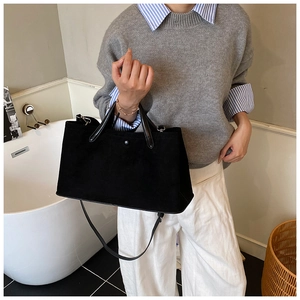 Detailed side view of black suede tote bag with leather strap on a model indoors