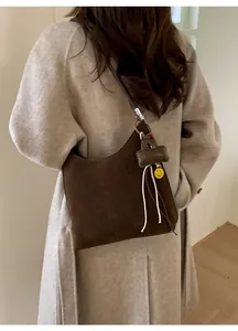 Detail of dark brown suede hobo bag with smile pendant worn on shoulder by a model